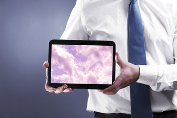 Businessman holding tablet PC with sky in screen. Cloud computing concept