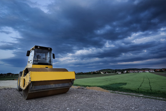 Radwalze auf Baustelle mit Abendhimmel und Siedlung
