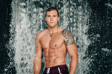 muscled  young man under the waterfall