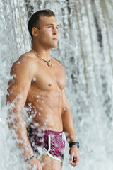 muscled  shirtless young man under the waterfall