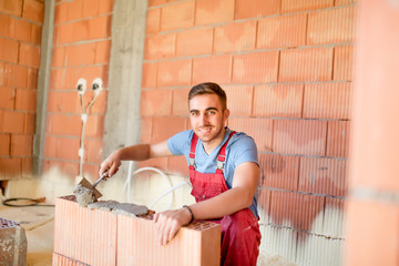 smiling worker building brick walls with cement, mortar and putty knife. Mason using mortar for...