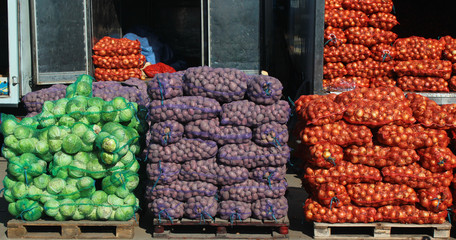 Piles of mesh sacks with fresh cabbage potatoes and onions