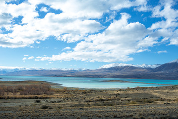 Fototapeta na wymiar Lake Tekapo in beautiful turquoise blue, that is caused by glacial flour, fine rock particles from the glaciers. The lake is dominant among brown dry grass, and dark-toned color of mountain ridges.