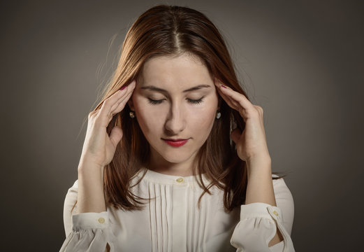 A young woman with a headache holding hands on her head, depression, pain, migraine, studio shot on gray background