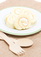 Sliced vanilla roll cake on plate with wooden spoon and sackclot