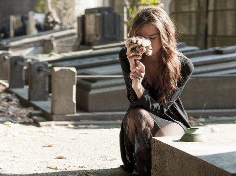 Sad woman holding bunch of flowers near a grave