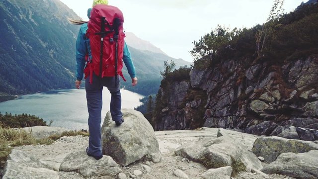 Hiker woman standing with hands up achieving the top, admiring mountain lake landscape. Stabilized Slow Motion 120 fps. Epic Steadicam hiking in stormy wind, success concept. Misty Mountains Series. 