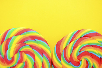 Fototapeta na wymiar Rainbow lollipop candy on bright yellow wood table.