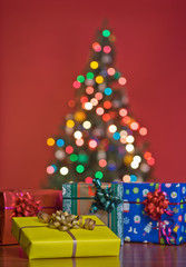 Gifts and multi colour Christmas tree bokeh in a red background