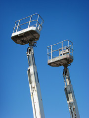 two industrial boom lift basket and arm rising into blue sky