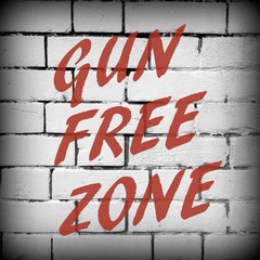 The words Gun Free Zone in red text on a brick wall background processed in black and white for...