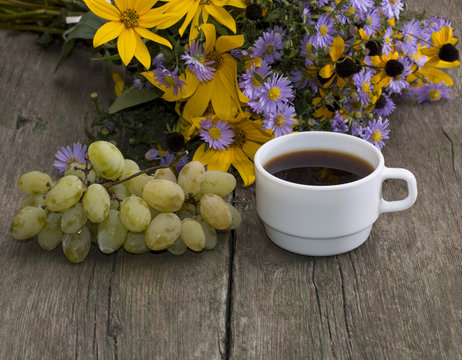cluster of grapes, coffee and bouquet of wild flowers on a woode