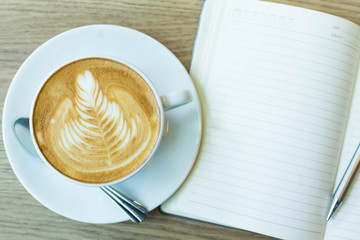 Hot latte art coffee cup on wooden table and note book, vintage