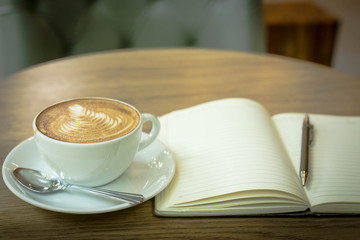 Hot latte art coffee cup on wooden table and note book, vintage