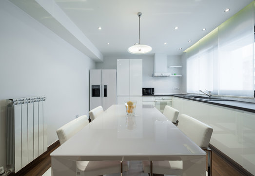 Interior of a modern luxury bright white kitchen with dining tab