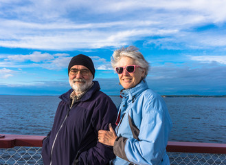 man and woman smiling, enjoying the view from the deck of lake cruise ship 
