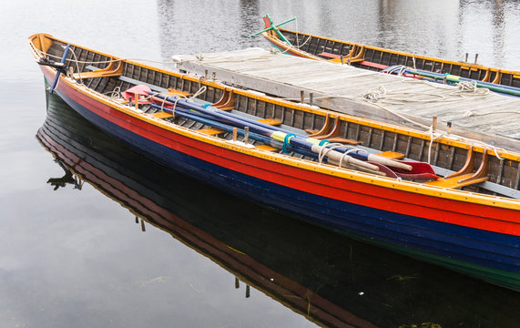 two colorful wooden,row boats tied up at pier with long oars for team rowing 