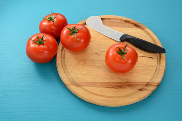 Four tomatoes on a chopping board with a knife