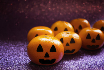 Orange mandarins in the form of a pumpkin painted in the form of icons of Halloween on the brilliant purple background closeup