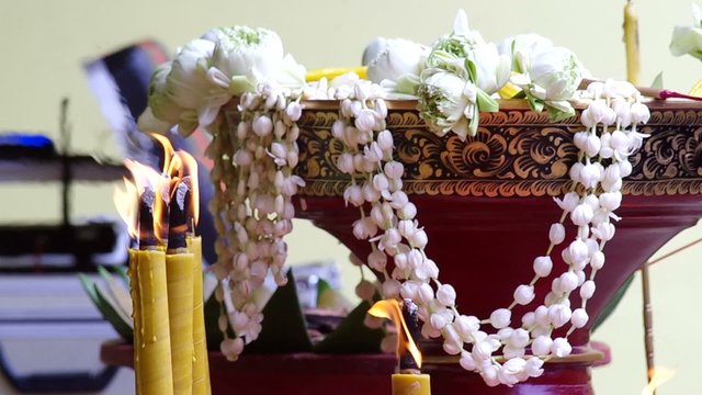 burning candle in front of the jasmine flower garland in the tray