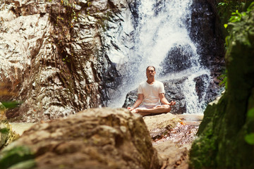 Fototapeta na wymiar sporty young man practicing yoga near a waterfall in the mountai