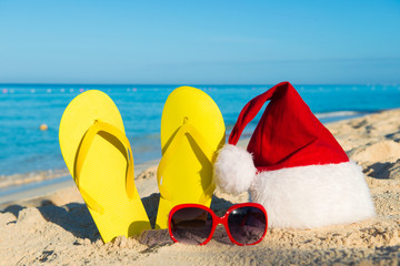 Obraz premium Christmas vacation at sea. Happy New Year holidays. Santa hat, sandals, sunglasses on sandy beach