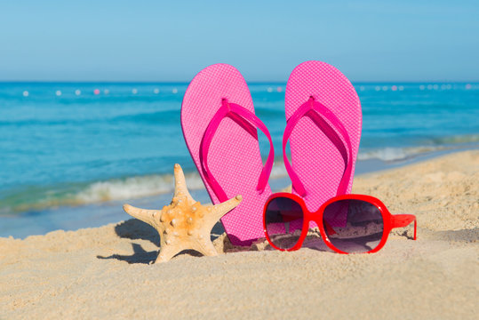 The sea, beach, sand and women's accessories: pink flip-flops, red sunglasses and starfish