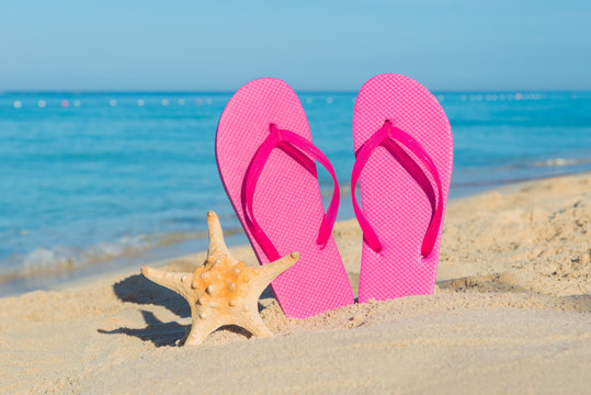 Travel by sea. Beach vacation. Pink flip-flops and starfish on sandy seashore.
