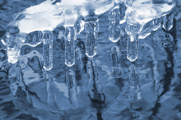 Ice transparent icicles on the river with reflection