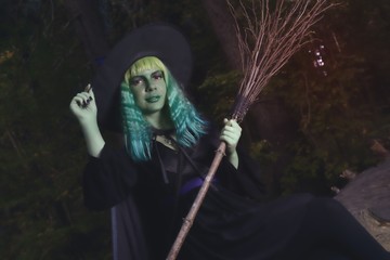 Young girl with green hair and broom in suit of witch in forest. Halloween time