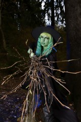 Young girl with green hair and broom in suit of witch in forest. Halloween time