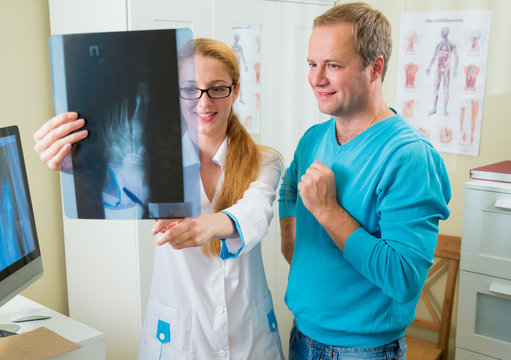 Smiling female doctor with handsome male patient looking at x-ray at office. Doctor talking to her patient and showing radiograph.