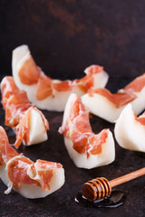 Melon with Serrano ham,sliced with honey on a black background.
