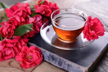 Old book with beautiful flowers and cup of tea on wooden table close up