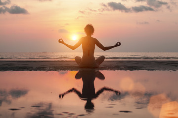 Woman doing meditation on the Sea beach. Yoga silhouette.