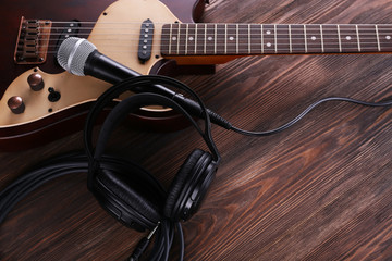 Electric guitar with microphone and headphones on wooden table close up