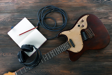 Naklejka premium Electric guitar with headphones and notebook on wooden table close up