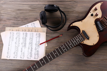 Naklejka premium Electric guitar with headphones and music notes on wooden table close up