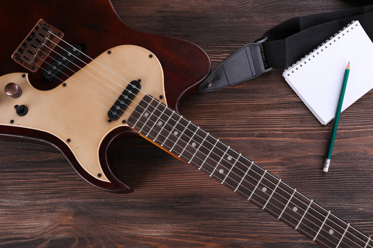 Electric guitar with notebook on wooden table close up