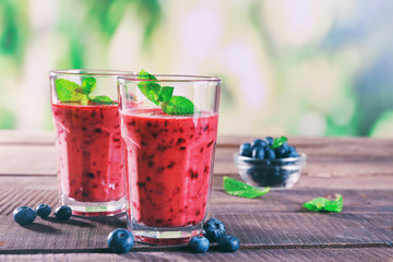 Glasses of berry smoothie on wooden table on blurred background