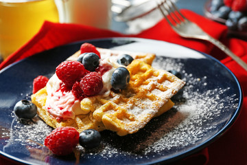 Sweet homemade waffles with forest berries and cream on plate, on dark wooden background