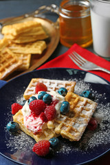 Sweet homemade waffles with forest berries and cream on plate, on dark wooden background