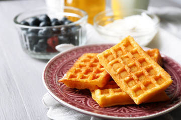 Sweet homemade waffles on plate, on color wooden background