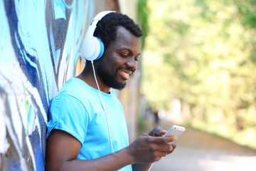 African American man listening music with headphones near graffiti wall outdoors