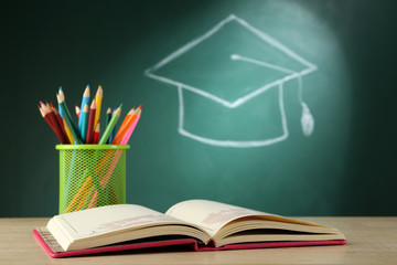 Metal cap of crayons with open book and bachelor hat drawing on blackboard background