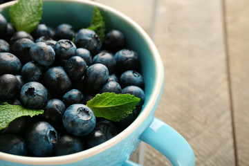 Fresh blueberries in cup on wooden table close up