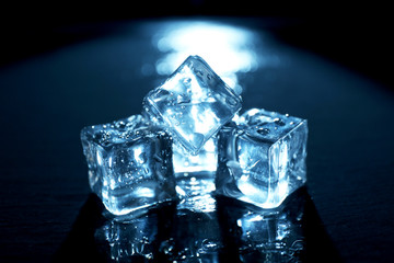 Shining ice cubes under blue light on liquid background