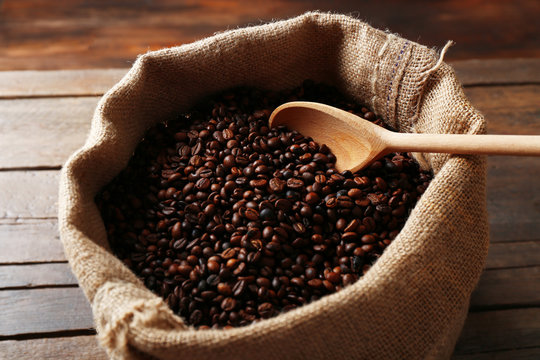 Sac with roasted coffee beans with spoon on wooden background © Africa Studio