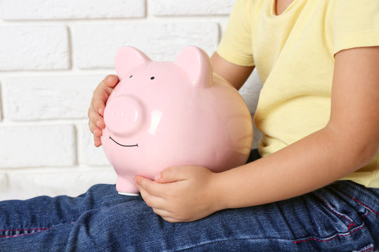 Little girl with the pig  moneybox on brick wall background