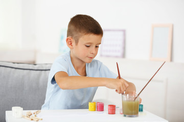 Cute little boy painting picture on home interior background